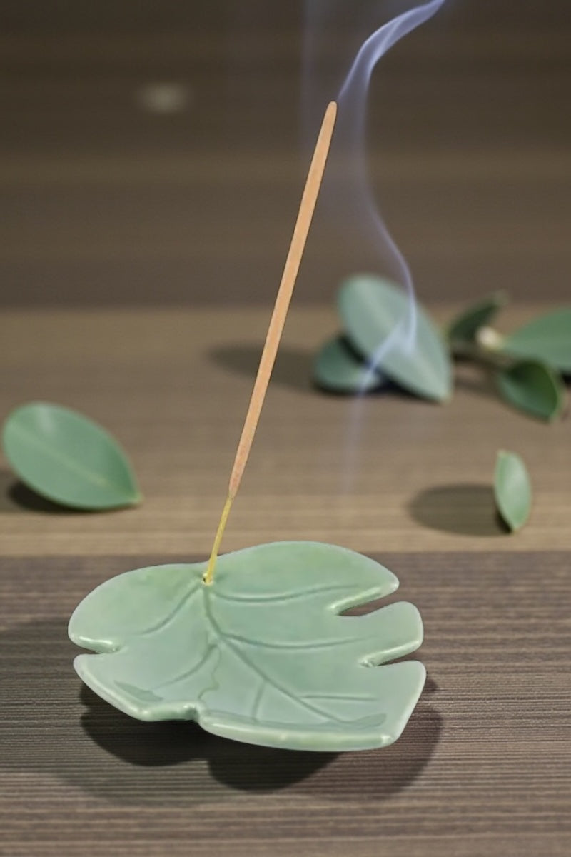 Incense stick on a leaf-shaped green holder with smoke on a wooden surface